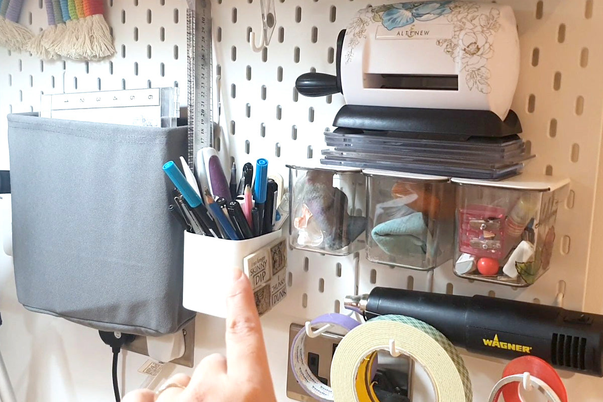 A white wall mounted pegboard with hooks and bins filled with crafting supplies and tools