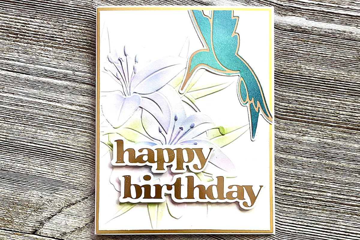 A birthday card with a floral background and hummingbird design created through hot foiling