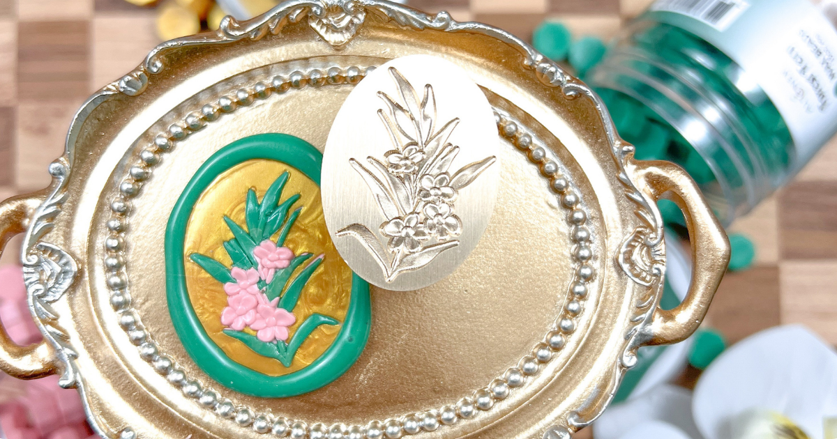 Staged photo of a wax seal and a wax seal stamp, with a few different wax bead colors in the background