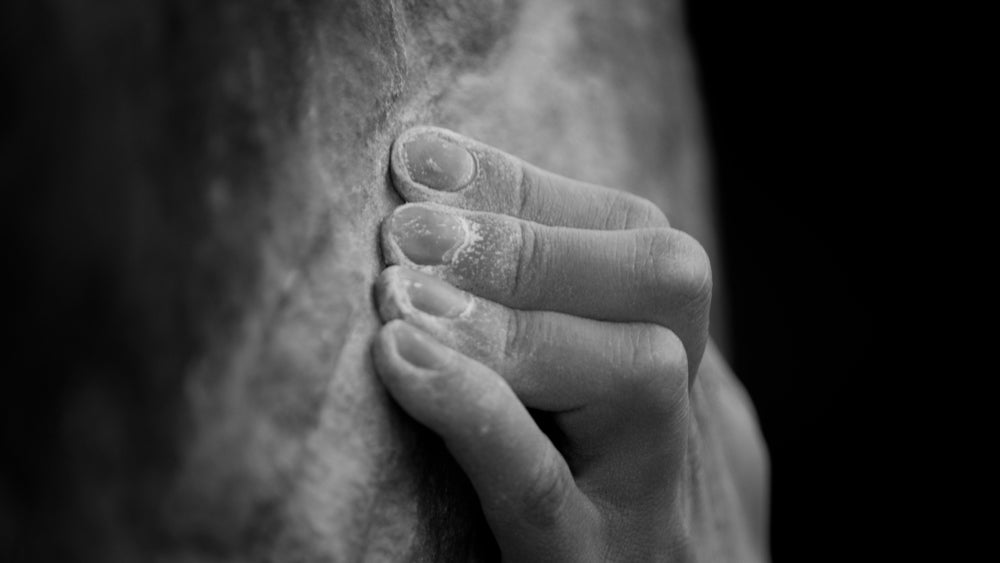 A climbers hands, covered in chalk crimping on a thin ledge