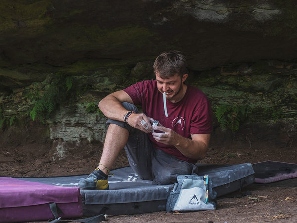 man using rock climbing finger tape sat on a bouldering crash pad next to a bouldering chalk bag