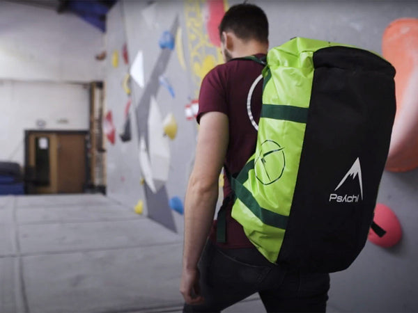 climber approaches indoor bouldering wall with rock climbing duffle bag over his shoulder