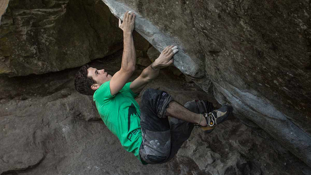 A climber is bouldering on a rock with climbing tape stapping on his fingers