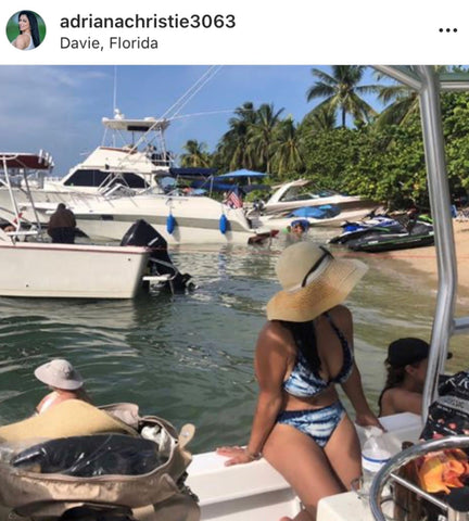 Instagram post of woman sitting on a boat at the beach wearing a hat and a blue bikini.