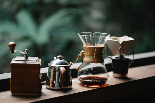 Chemex coffeemaker with cup placed on terrace with metal kettle and hand grinder