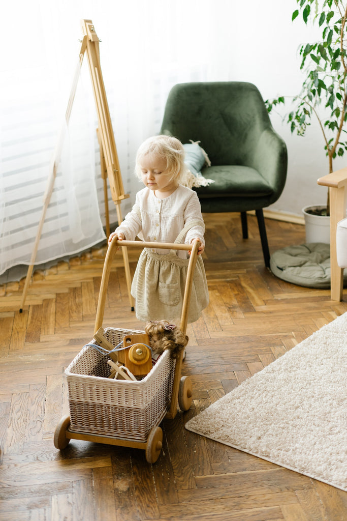 Cute little girl carrying wicker trolley with toys