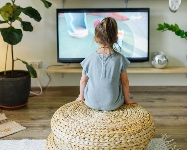 Faceless girl watching TV on wicker stool at home