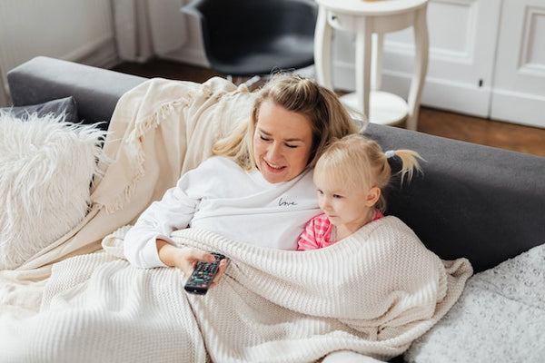 A mother and her child share blankets on a couch