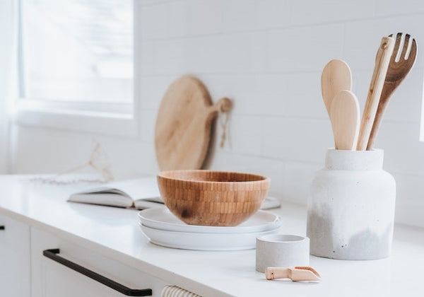 Wooden bowl and wooden kitchen utensils sit on a white counter