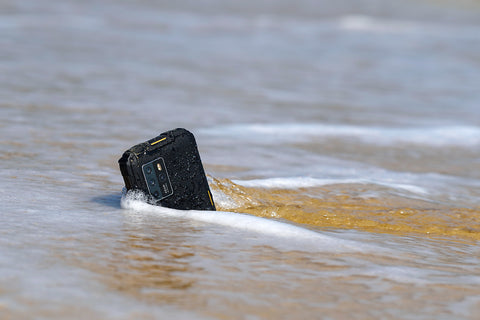 Oukitel WP10 5G rugged phone is partially buried and the sea water is retreating into the sea around it