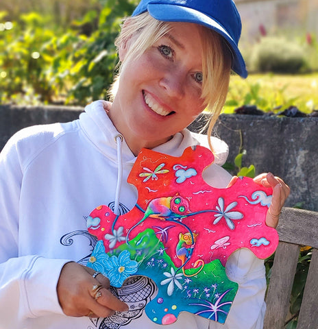 megan aroon holding an original puzzle piece painting of a colorful tarsier