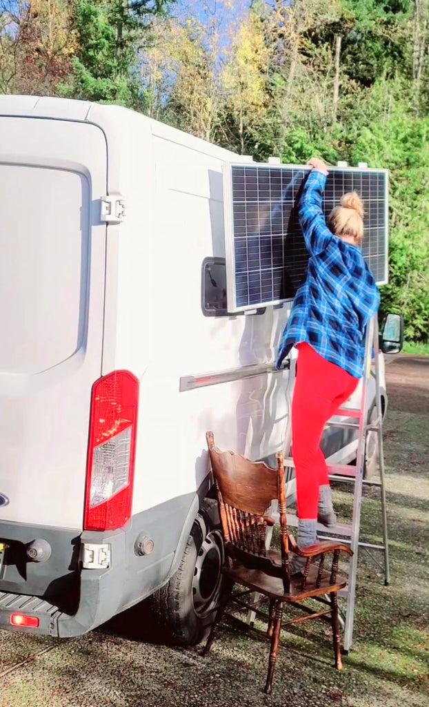 climbing onto the top of my van with a solar panel in hand as I self convert my van, how to do your own solar battery setup meganaroon