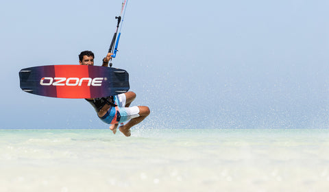 Kitesurfer performing a jump and can be seen smiling above the top of the Ozone Code V3 kitesurf board