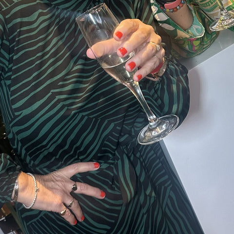 Lady wearing Burning Love nail polish holding a glass of champagne in a green animal print dress