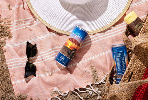 Beach Bum Blueberry sparkling wine can on the beach with sunglasses and beach hat.