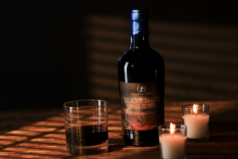 A bottle of Tanglewood Winery's Bourbon Barrel Blue Blood on the table next to a glass of wine and two candles.