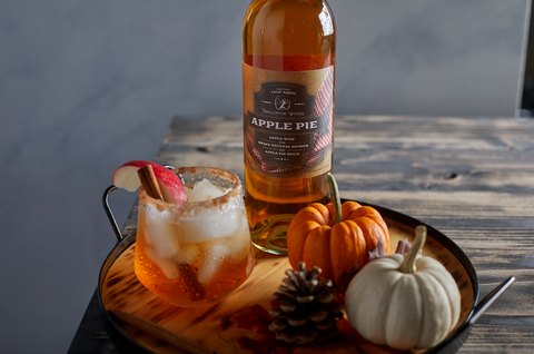 A freshly made Apple Pie Old Fashioned sits next to a full bottle of Tanglewood Winery's Apple Pie wine and two small pumpkins.