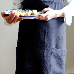 Person holding plate with food and wearing Annie Linen Smock Apron in Ink Blue 