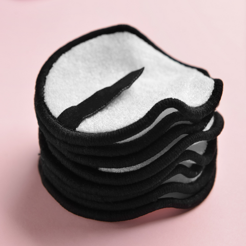 Round white reusable make-up pads with black stitching around the edge on a pale pink background.