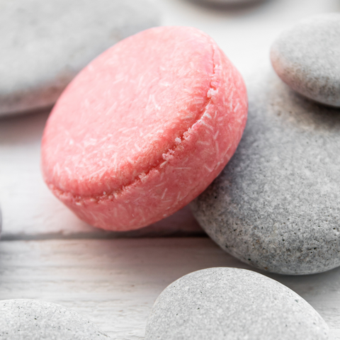 Close up of a pink Shampoo bar on a pale grey table with grey rocks.