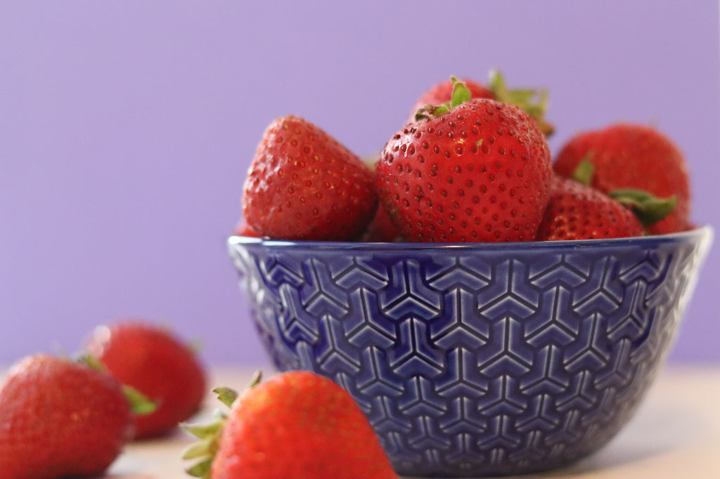 Photo of strawberries in a blue bowl with a blue background