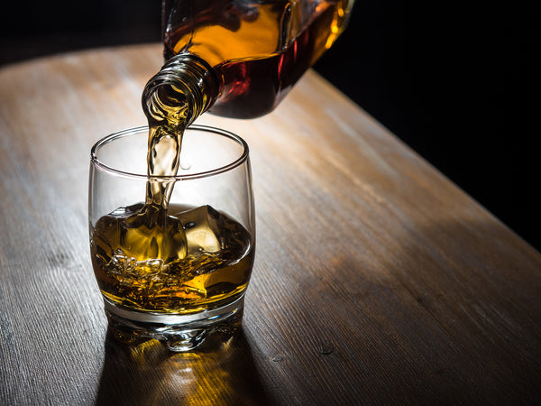 someone pouring whiskey into a glass with ice