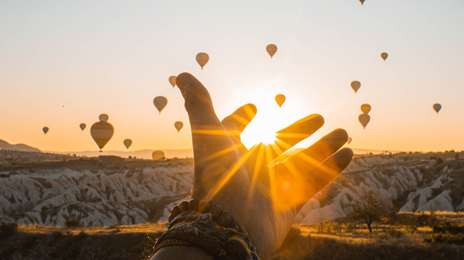 Persons open hand reaching towards a sunset sky filled with hot air balloons
