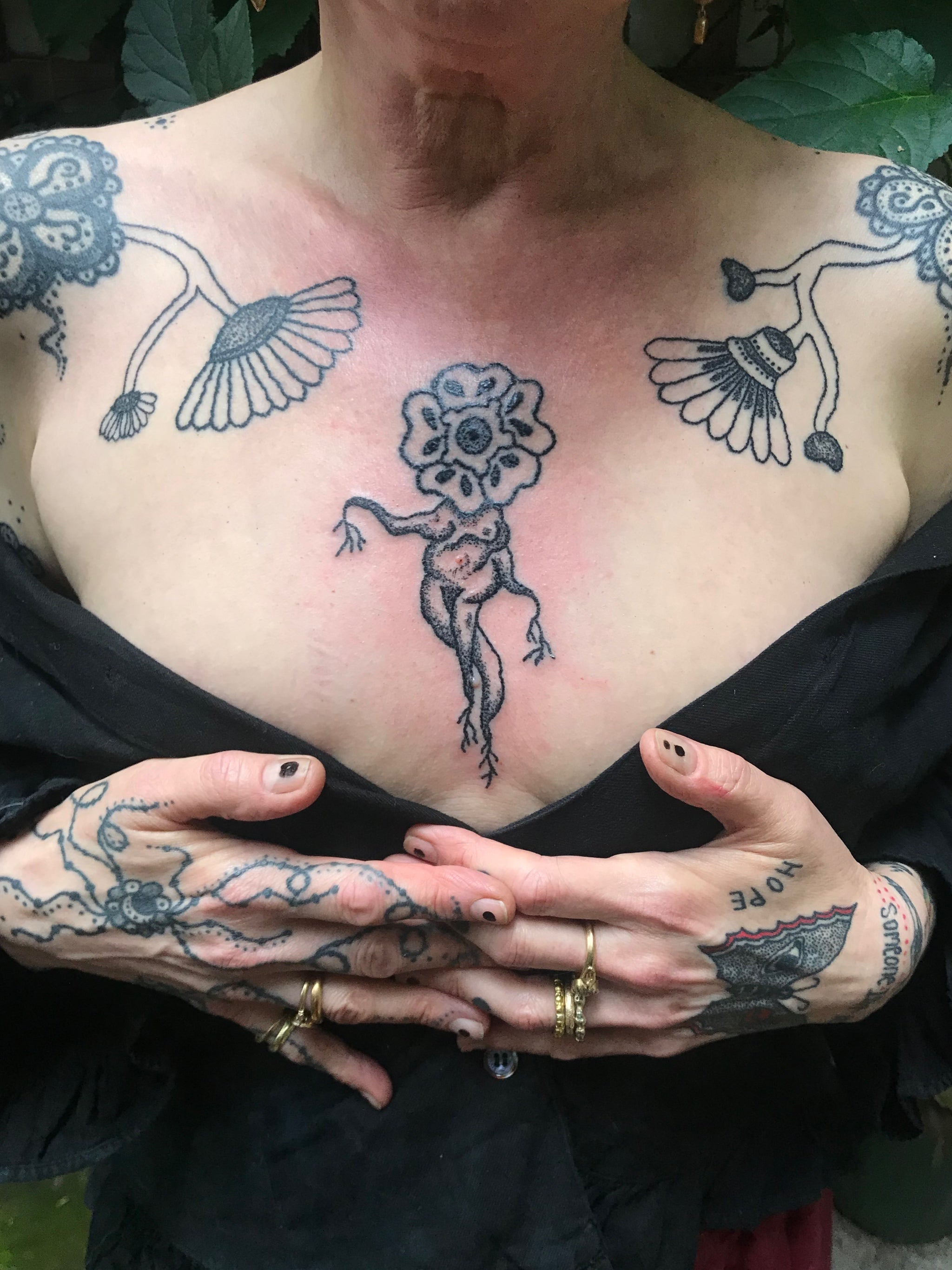 Woman with her hands at her bust showing off her black tattoos on her chest