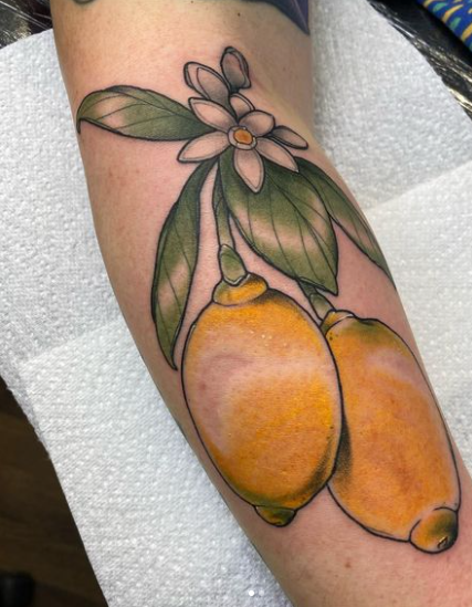 Tattoo of two yellow lemons with leaves and white flower on a arm