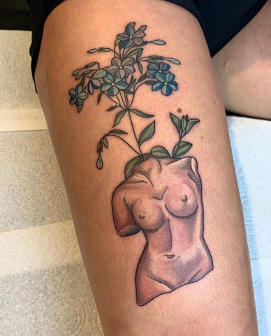 The tattoo shows the headless torso of a woman with foliage growing from her neck tattooed on a leg.