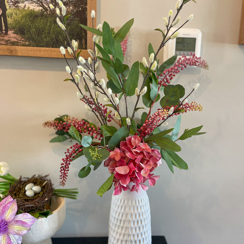 A silk floral design with eucalyptus and hydrangea sits on an entry table