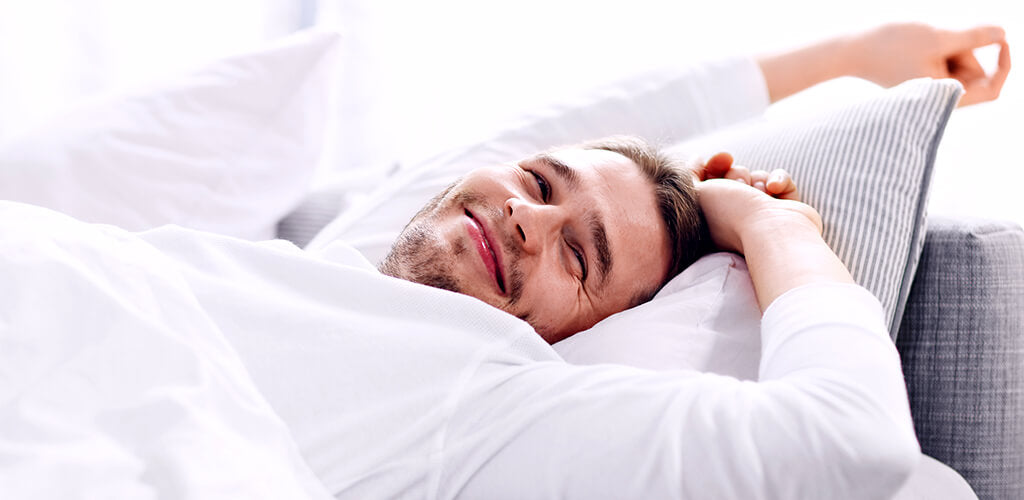 Junger Mann erwacht ausgeschlafen, erholt und glücklich im Bett