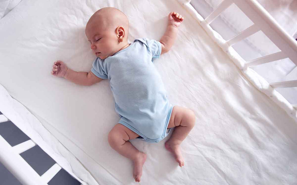 Schlafendes Baby auf dem Rücken im Bett