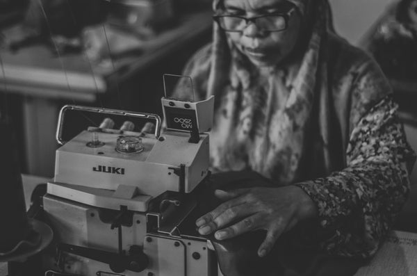 A black and white photograph of a woman working on a sewing machine to create sustainable and ethical products for the fashion industry