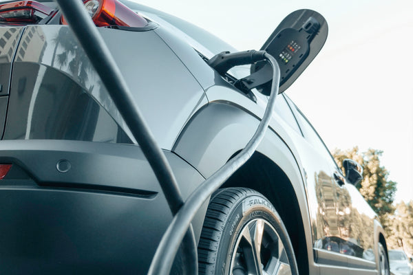 A gunmetal electric car on a summer day being charged with a cable.