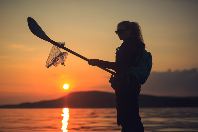 A woman holding up a piece of litter with a paddle at sunset