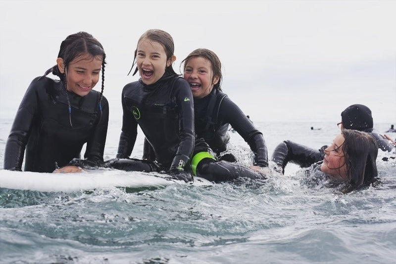 A group of kids sat on a surfboard in the sea laughing