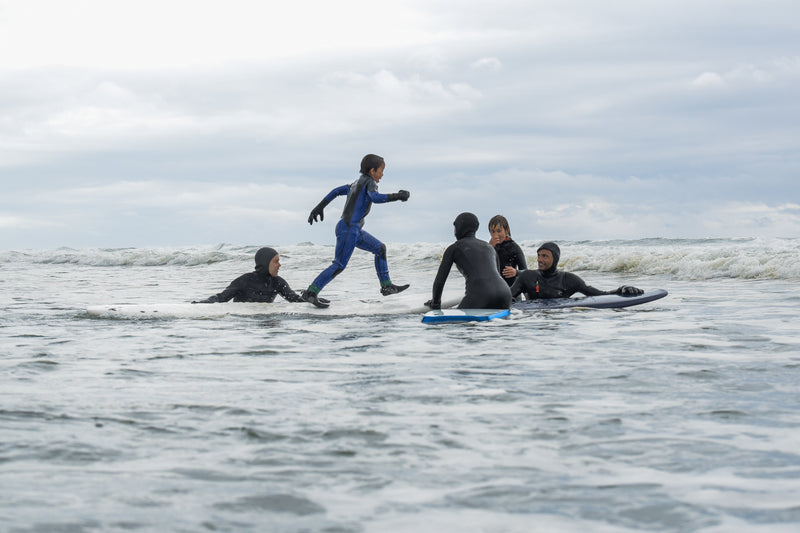 A group of surfers in the water with a kid running from board to board