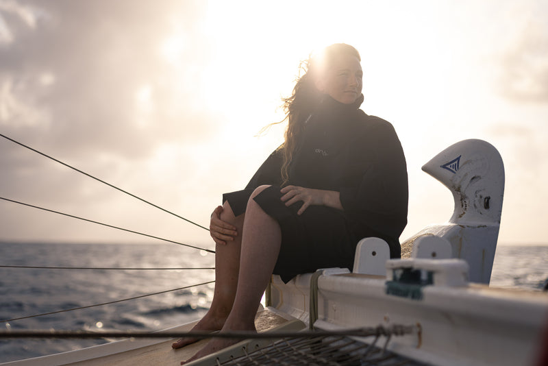 A woman sat on a boat at sea wearing a dryrobe Lite