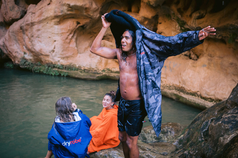 A man changing into a dryrobe by a natural pool of water