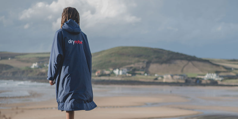 Man stood on beach wearing Navy dryrobe Advance featuring the new dryrobe logo