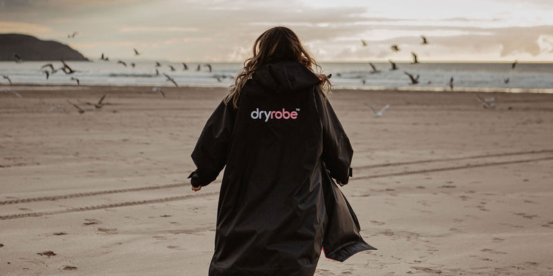 Woman on a beach wearing a dryrobe Advance with the new logo