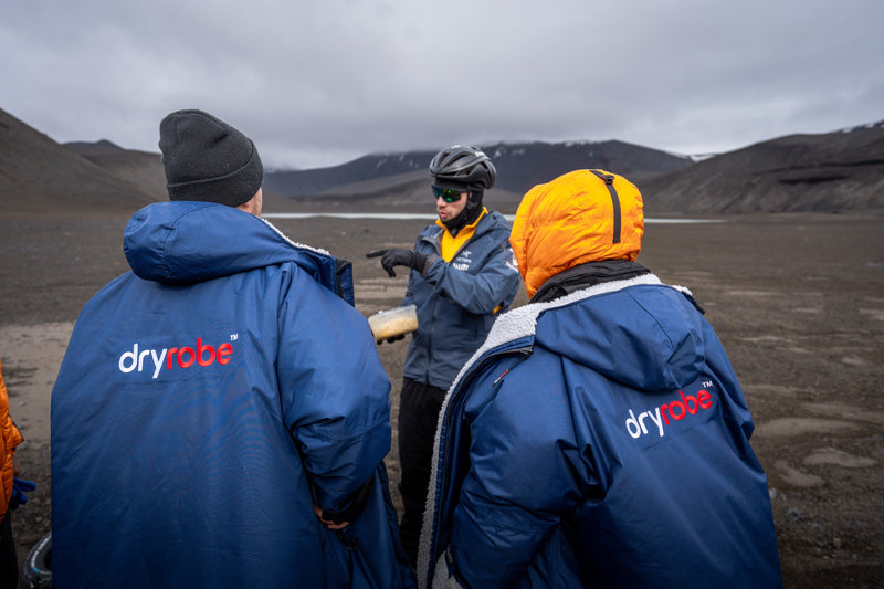 1 person stood by a bike holding a box of food with two people in dryrobes