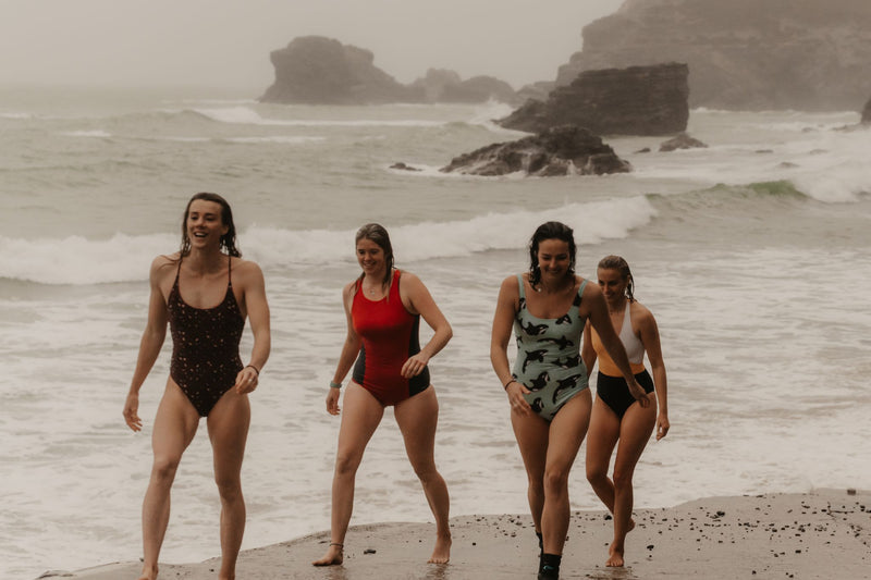 A group of female swimmers in swimming costumes walking on the beach