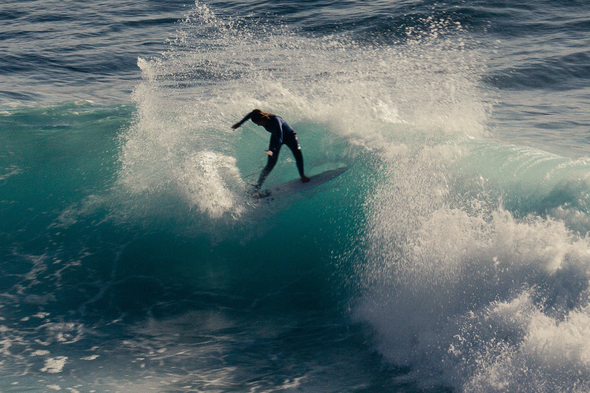 A shot Camilla Kemp surfing in a wetsuit taken from a distance