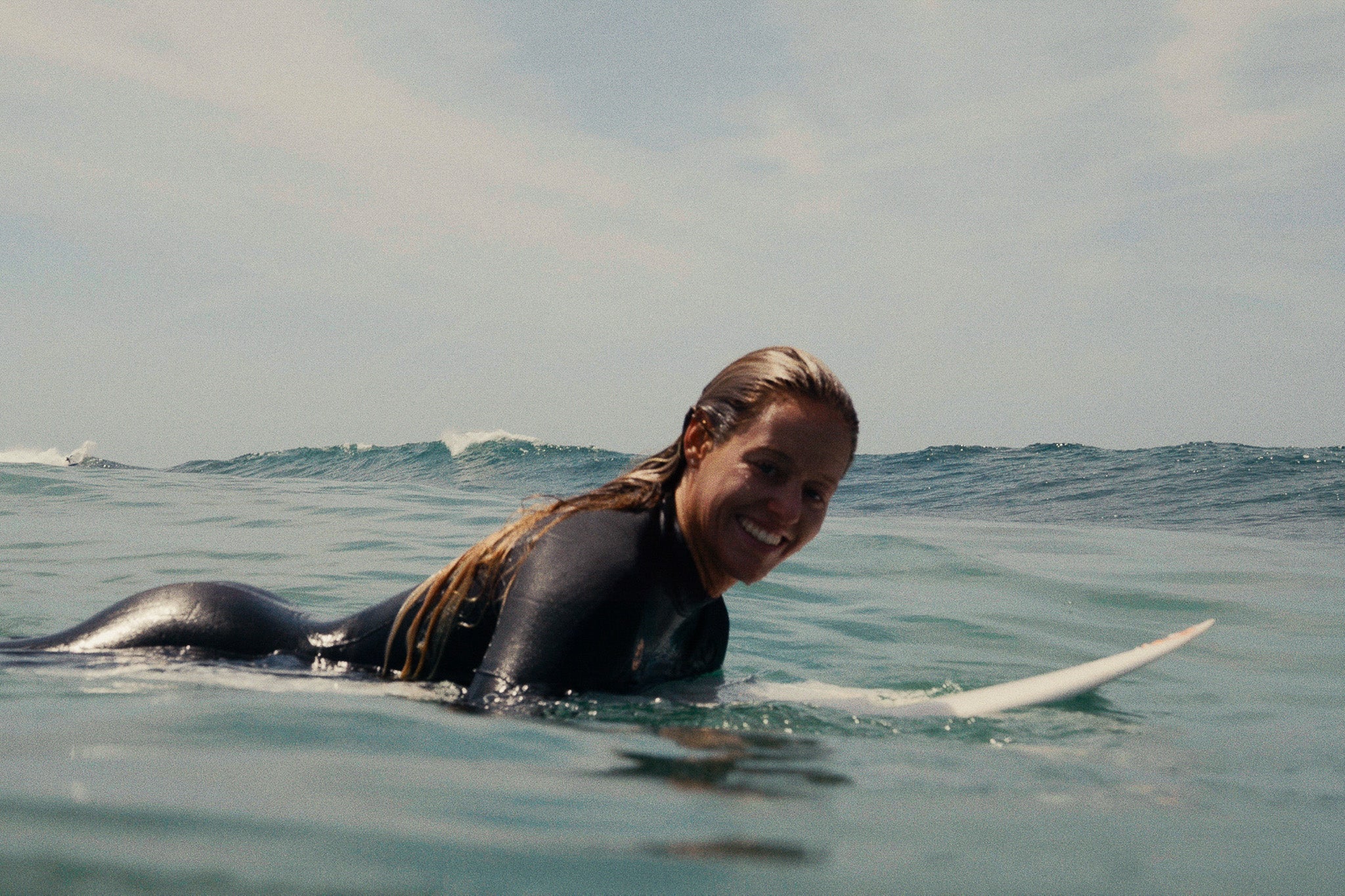 Camilla Kemp smiling whilst lying on her her surfboard in the ocean