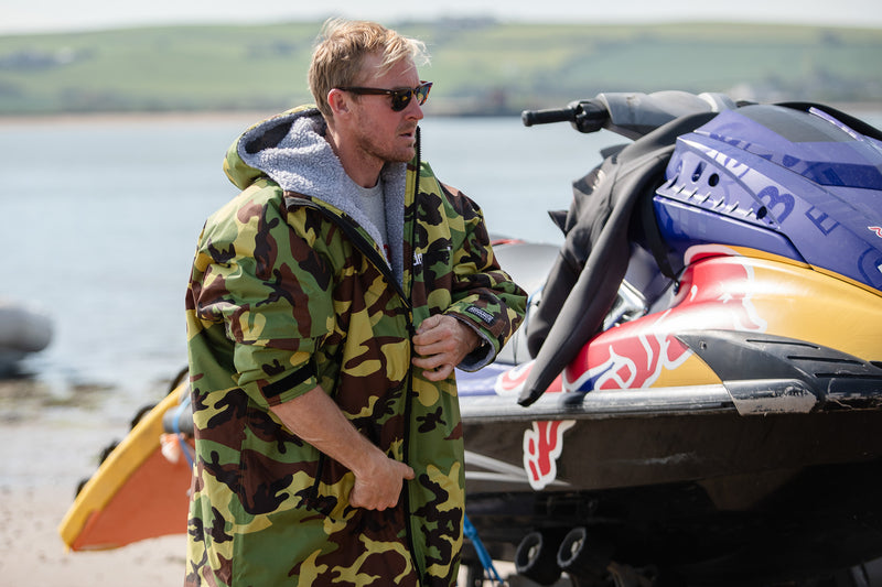 Andrew Cotton wearing a camo dryrobe Advance on the beach next to a jet ski