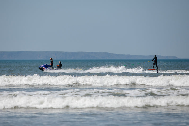 Andrew Cotton on a foiling board being towed in the water by a jet ski