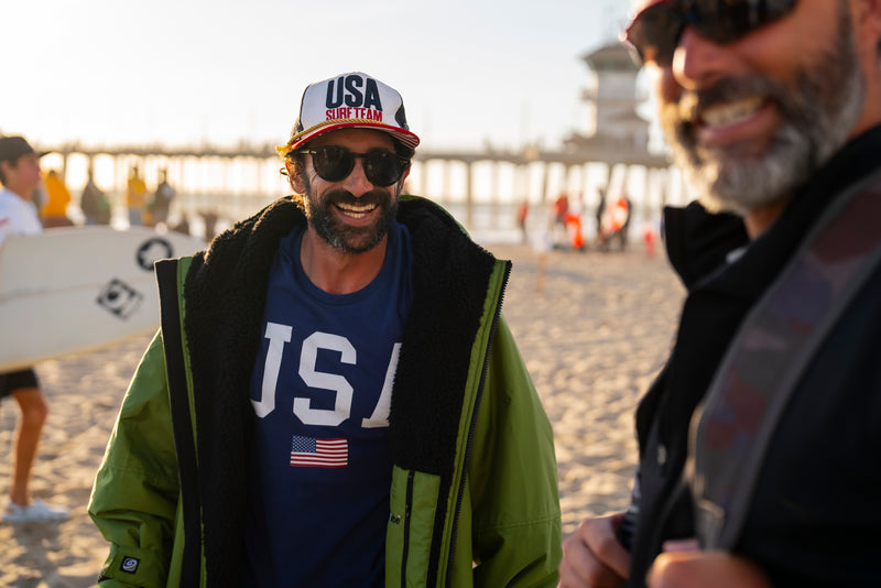 A man in a cap smiling on the beach in a dryrobe