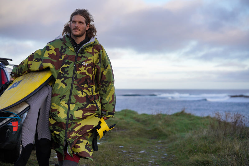 Taz Knight wearing a camo dryrobe Advance whilst carrying his surfboards